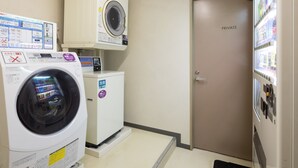 Une buanderie équipée d’un lave-linge et d’un sèche-linge à chargement frontal, dotée d’une porte privative et d’un distributeur automatique de boissons.