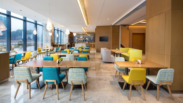 A modern dining area with multiple tables and chairs, large windows, and a television on the wall. - Holiday Inn Express Wuxi Taihu New City by IHG (Wuxi)