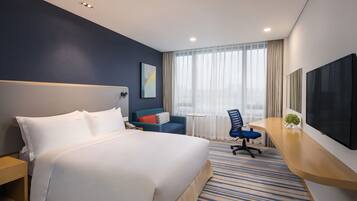 Une chambre d’hôtel avec un grand lit, un bureau avec une chaise, un téléviseur à écran plat et une fenêtre avec des rideaux.