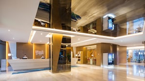 A modern hotel lobby with a reception desk, a digital information kiosk, and a seating area with a view of the city. - Holiday Inn Express Wuxi Taihu New City by IHG (Wuxi)