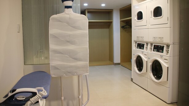 A laundry room with a large wall-mounted drying rack, a washing machine, and a bench with an iron. - Holiday Inn Express Wuxi Taihu New City by IHG (Wuxi)