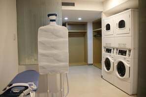 Een wasruimte met een groot wandrek, een wasmachine en een bank met een strijkijzer.
