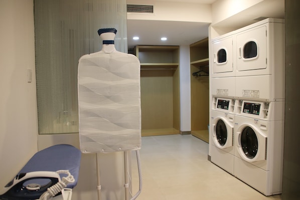 Uma lavanderia com um varal grande fixado na parede, uma máquina de lavar e um banco com um ferro.