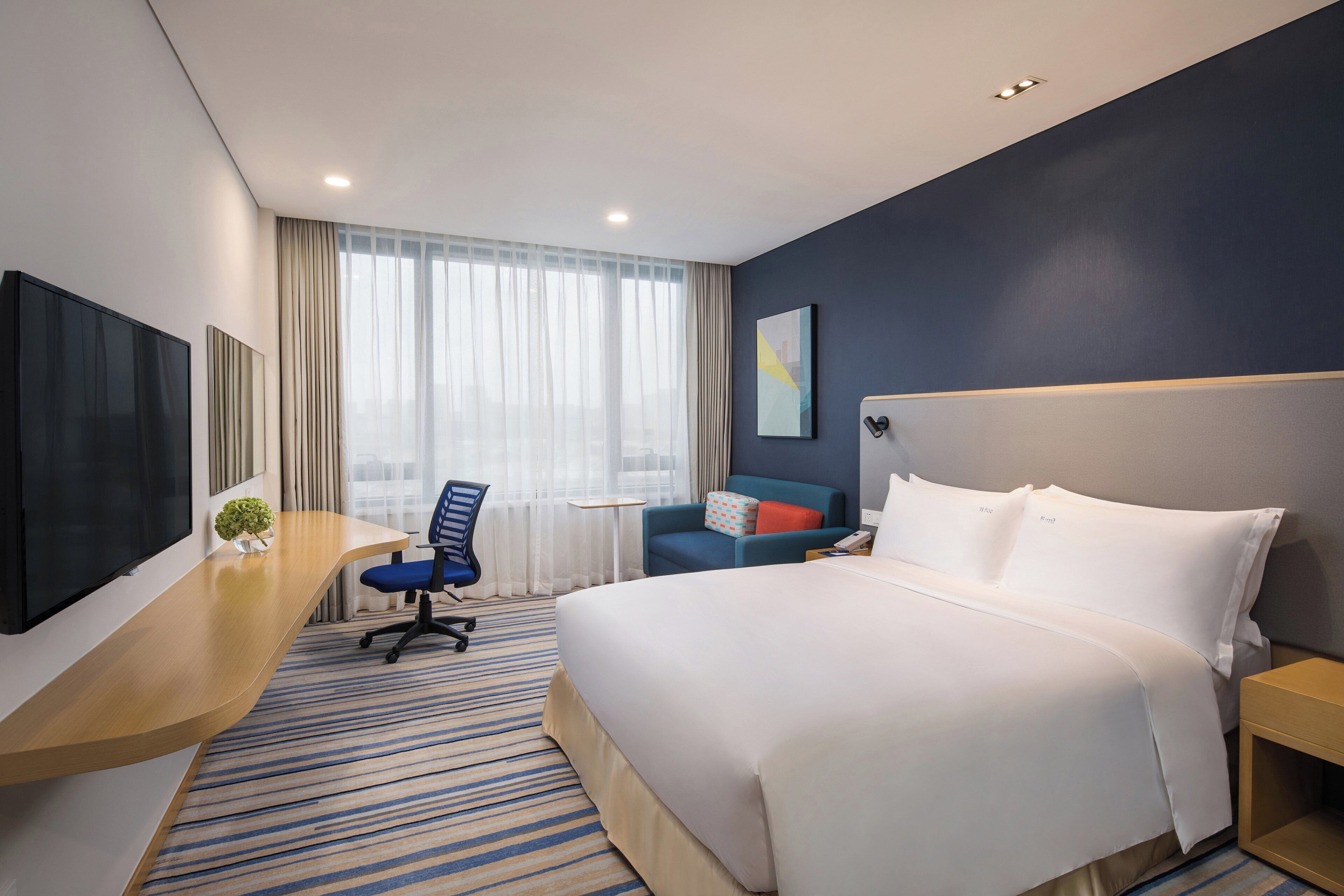 A hotel room with a bed, a desk, a chair, a TV, and a window with curtains.