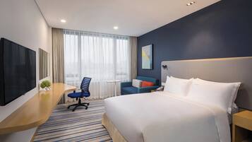 A hotel room with a bed, a desk, a chair, a TV, and a window with curtains.