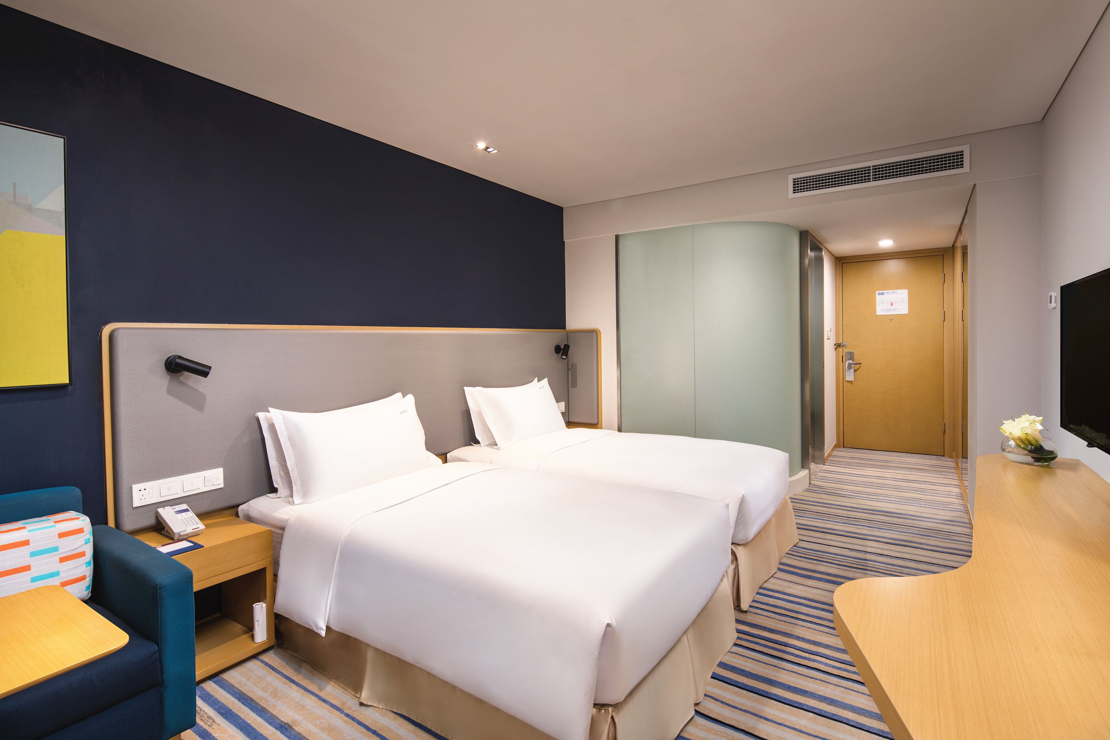 Habitación de hotel con dos camas, un escritorio, una silla, un televisor y un cuadro en la pared.