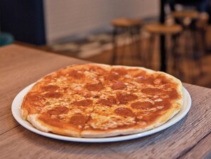 A pizza on a white plate on a wooden table. - Travelodge Birmingham Maypole (Birmingham)