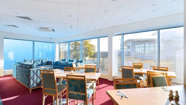 A modern dining area with large windows, a red carpet, and patterned furniture. - Travelodge Birmingham Maypole (Birmingham)