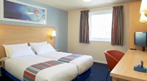 Une chambre d’hôtel comprenant un lit, un bureau avec une chaise, une télévision et une fenêtre avec des rideaux.
