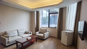 A living room with a sofa, armchair, coffee table, and a small refrigerator. - Vienna Hotel (Shenzhen Longzhu) (Shenzhen)