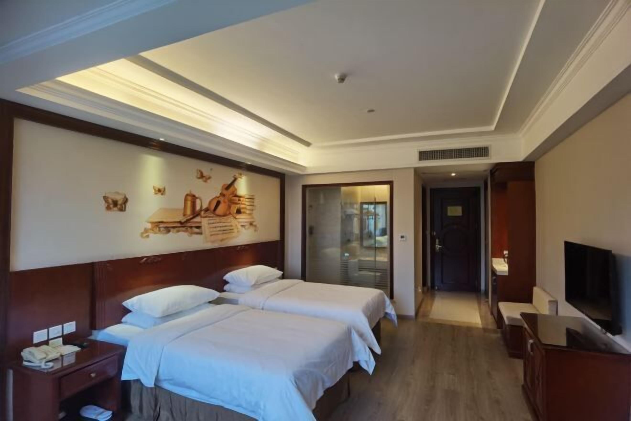 Une chambre d’hôtel avec deux lits, une télévision, un bureau et un tableau au mur.