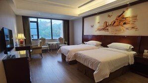 A hotel room with two beds, a TV, a desk with a lamp, a chair, a small table, and a large window with a view of the mountains. - Vienna Hotel (Shenzhen Longzhu) (Shenzhen)