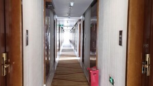 Un couloir d’hôtel avec un sol recouvert de moquette, des portes en bois et un panneau indiquant la sortie, bien visible.
