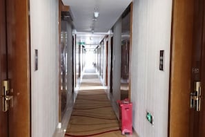 Un couloir d’hôtel avec un sol recouvert de moquette, des portes en bois et un panneau indiquant la sortie, bien visible.