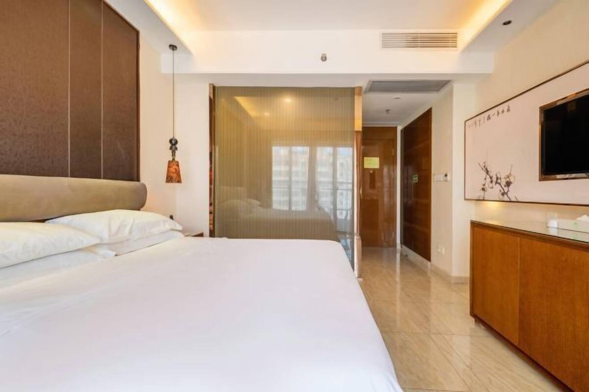 A hotel room with a large bed, a wooden headboard, a TV mounted on the wall, and a wooden cabinet.