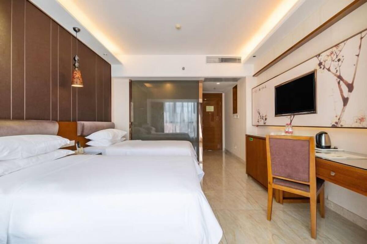 A hotel room with two beds, a desk, a chair, a television, and a wall-mounted artwork.