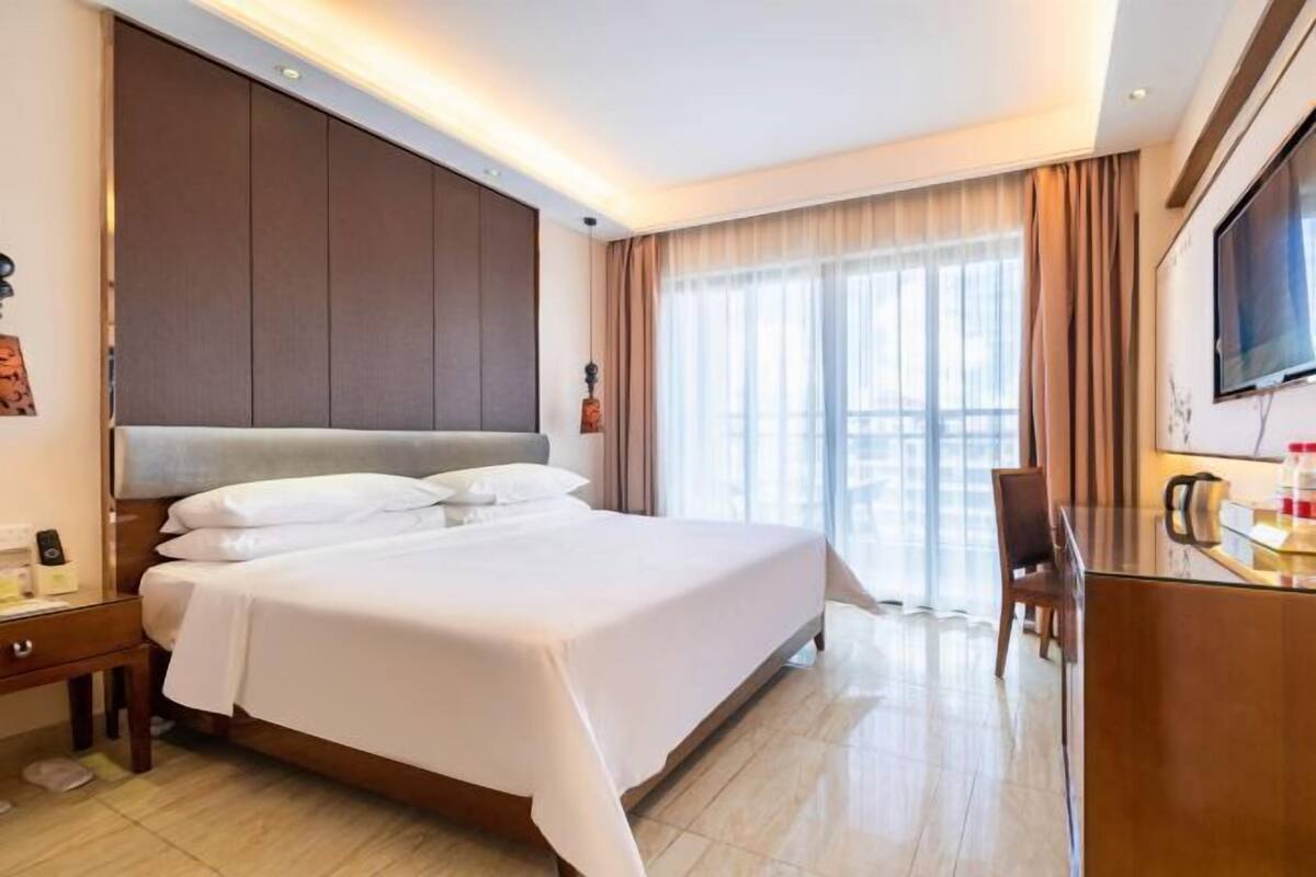 A hotel room with a large bed, a desk with a chair, a TV, and a window with curtains.