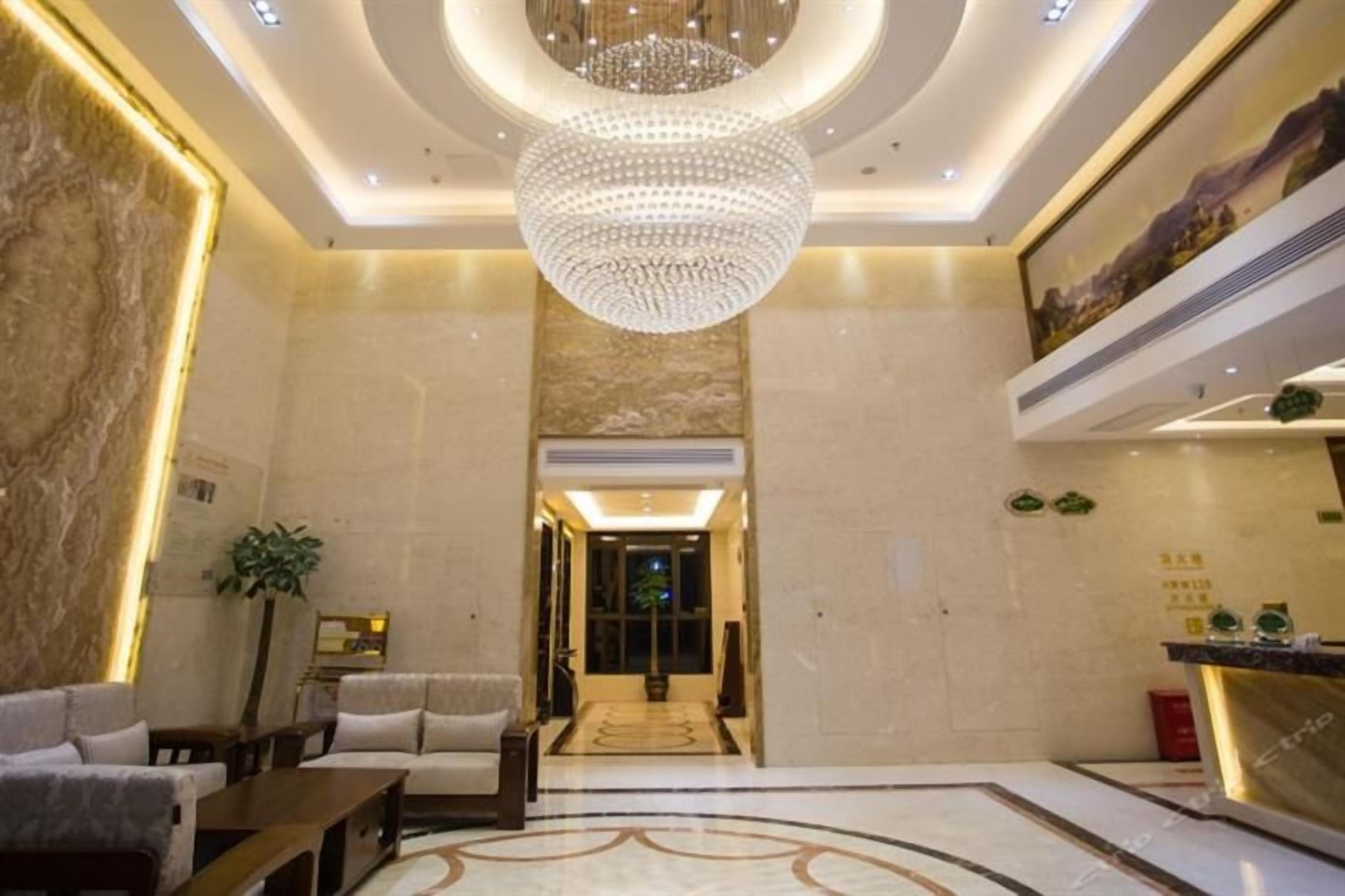 A hotel lobby with a chandelier, seating area, and a reception desk.
