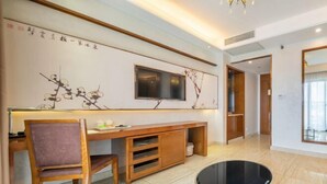 Un salon moderne avec un bureau en bois, une chaise, un téléviseur fixé au mur et une table basse ronde en verre.