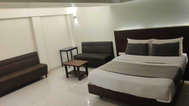 Una habitación de hotel con una cama grande, un sofá oscuro, una mesita pequeña y una lámpara en el techo.