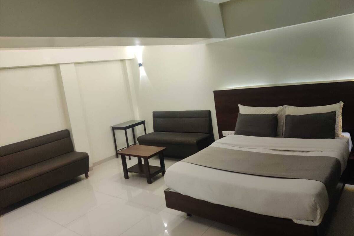 A hotel room with a large bed, a dark sofa, a small table, and a ceiling light.