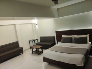 Une chambre d’hôtel avec un grand lit, un canapé sombre, une petite table et un luminaire au plafond.
