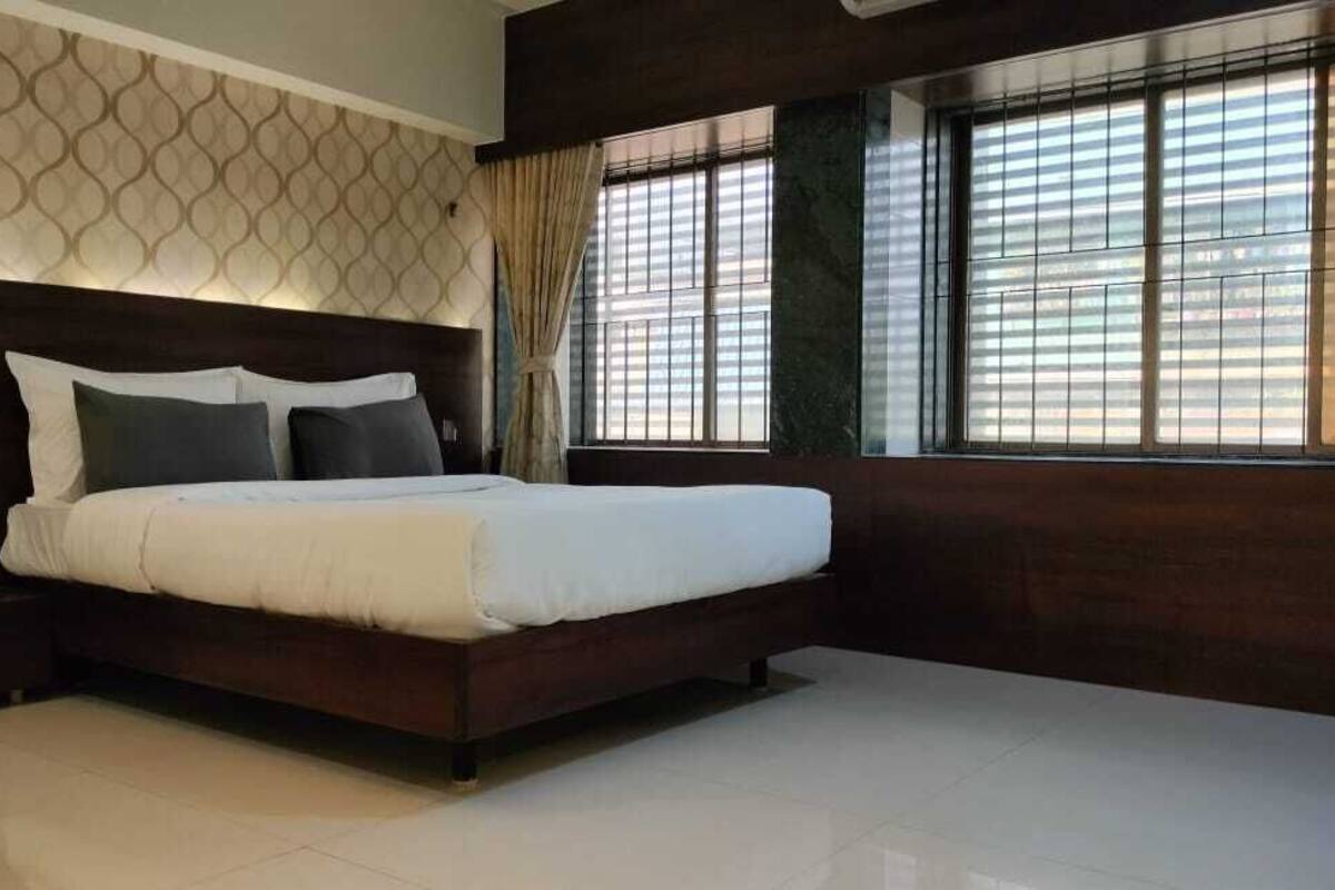 A modern hotel room with a large bed, a nightstand, a window with blinds, and a patterned wall.