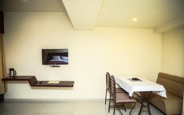 Une chambre d’hôtel avec un téléviseur fixé au mur, une petite table avec une chaise et un canapé.