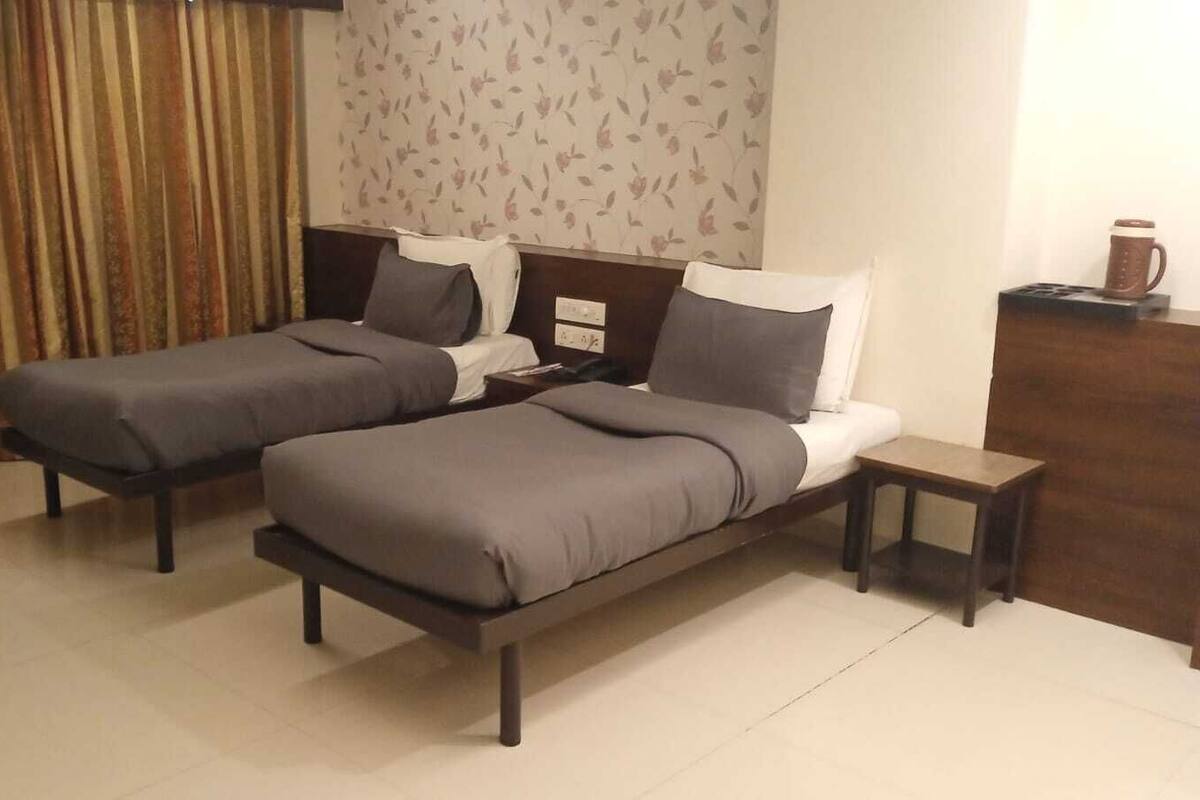 A hotel room with two single beds, a small bedside table, a nightstand, and a decorative wall panel.