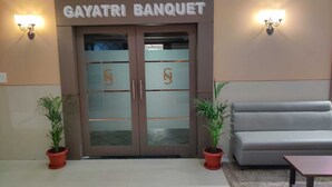 La entrada al Salón de Banquetes Gayatri, con un diseño moderno, presenta dos plantas en macetas y un sofá gris al frente.