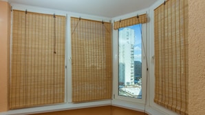 A corner room with three windows covered by bamboo blinds, a radiator, and a view of a tall building. - naDobu Hotel Poznyaki (Kyiv)