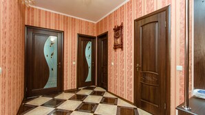A hallway with patterned wallpaper, checkered flooring, and wooden doors with glass panels. - naDobu Hotel Poznyaki (Kyiv)