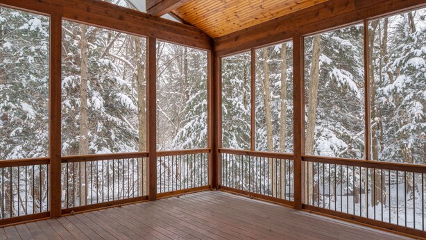 Una amplia terraza de madera con grandes ventanales que dan a un bosque nevado.