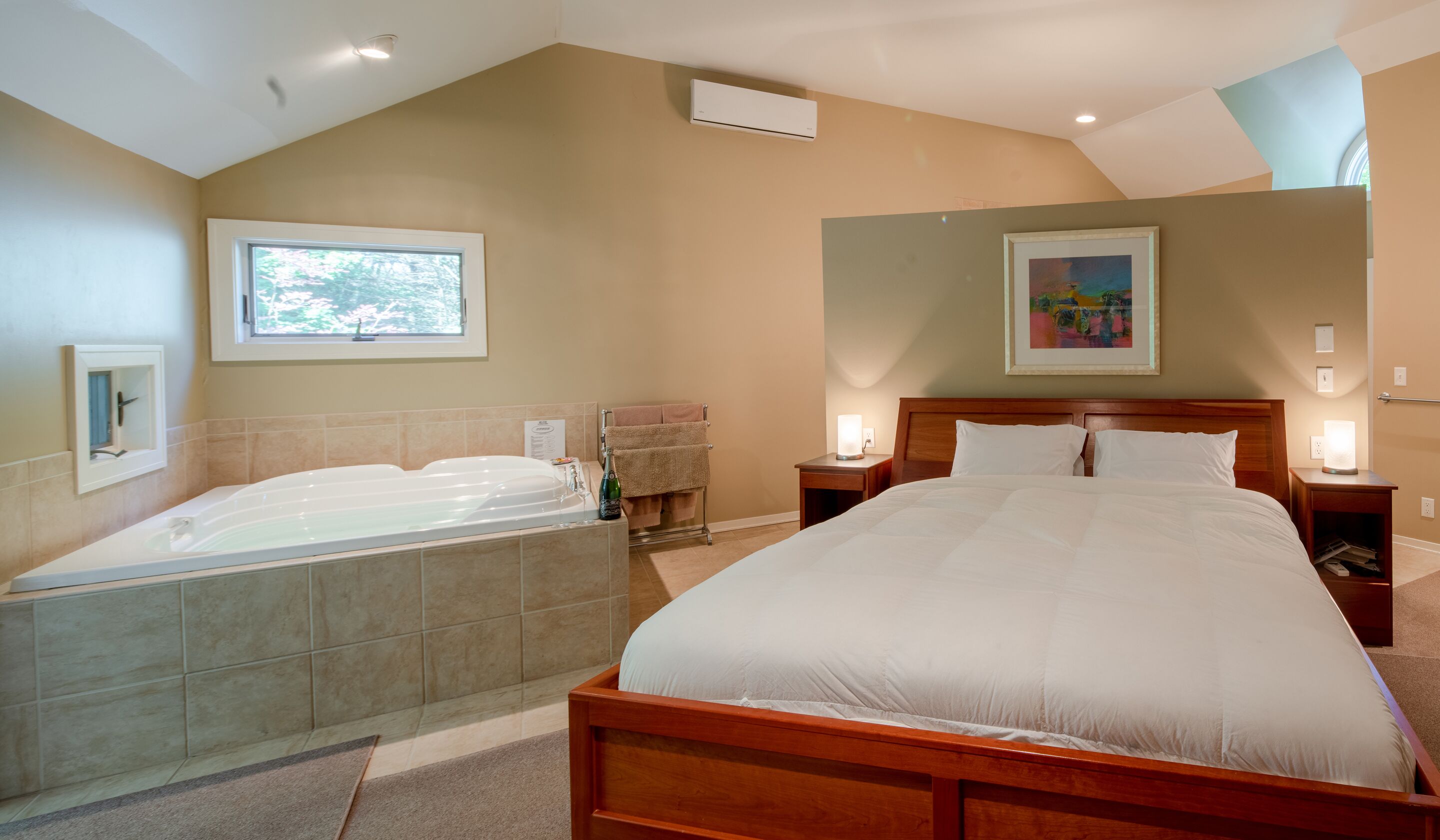 A bedroom with a large bed, a separate bathtub, a window, a painting, and a ceiling fan.