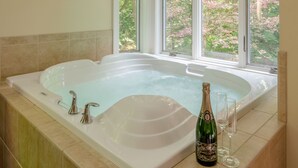 Una bañera grande con una botella de champán y copas, una ventana con vistas a árboles y un suelo de baldosas.