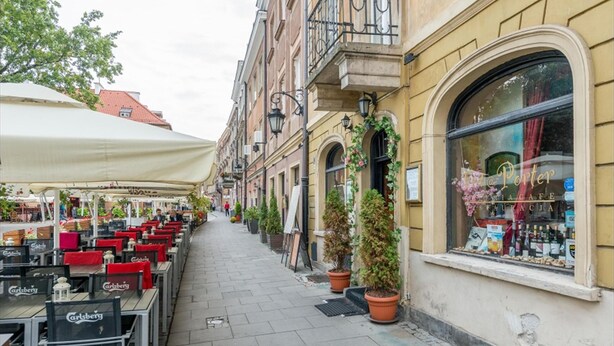 En smal gata med uteserveringar längs en caféfasad, och en byggnad med ett stort fönster och en skylt som visar texten "Café Porter".