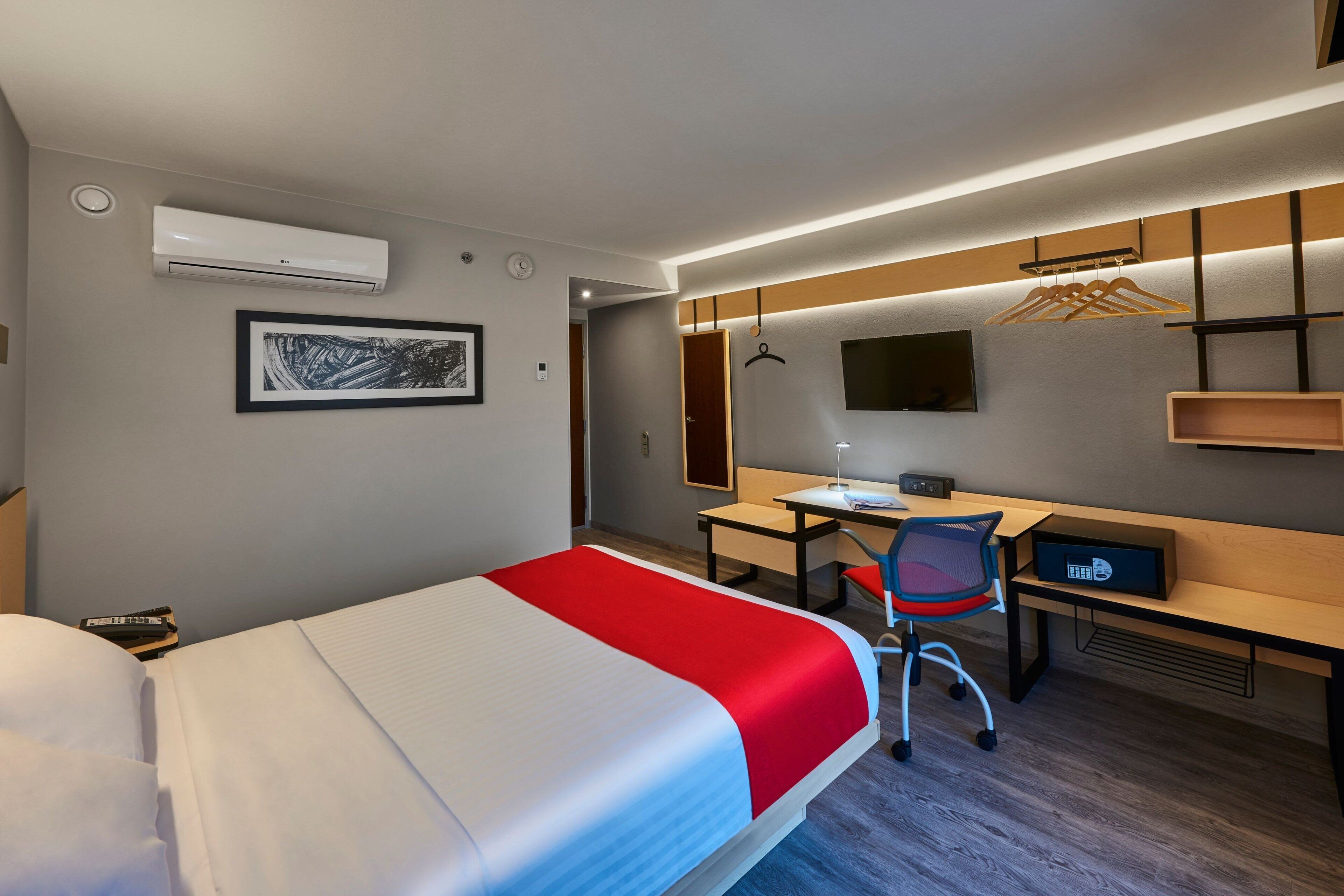 A modern hotel room with a bed, desk, chair, and a TV.