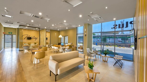 Een modern interieur met een bank, stoelen, tafels en een groot raam met uitzicht op buiten.