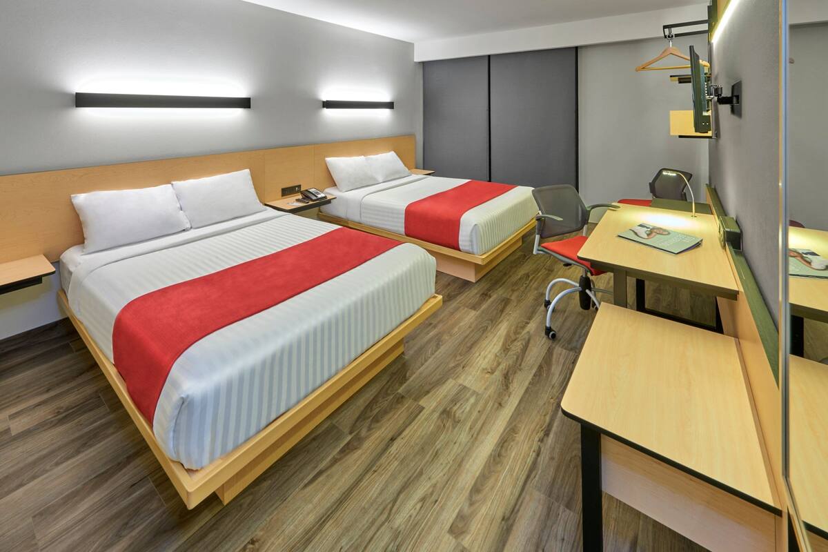 A hotel room with two beds, a desk, a chair, and a wardrobe.