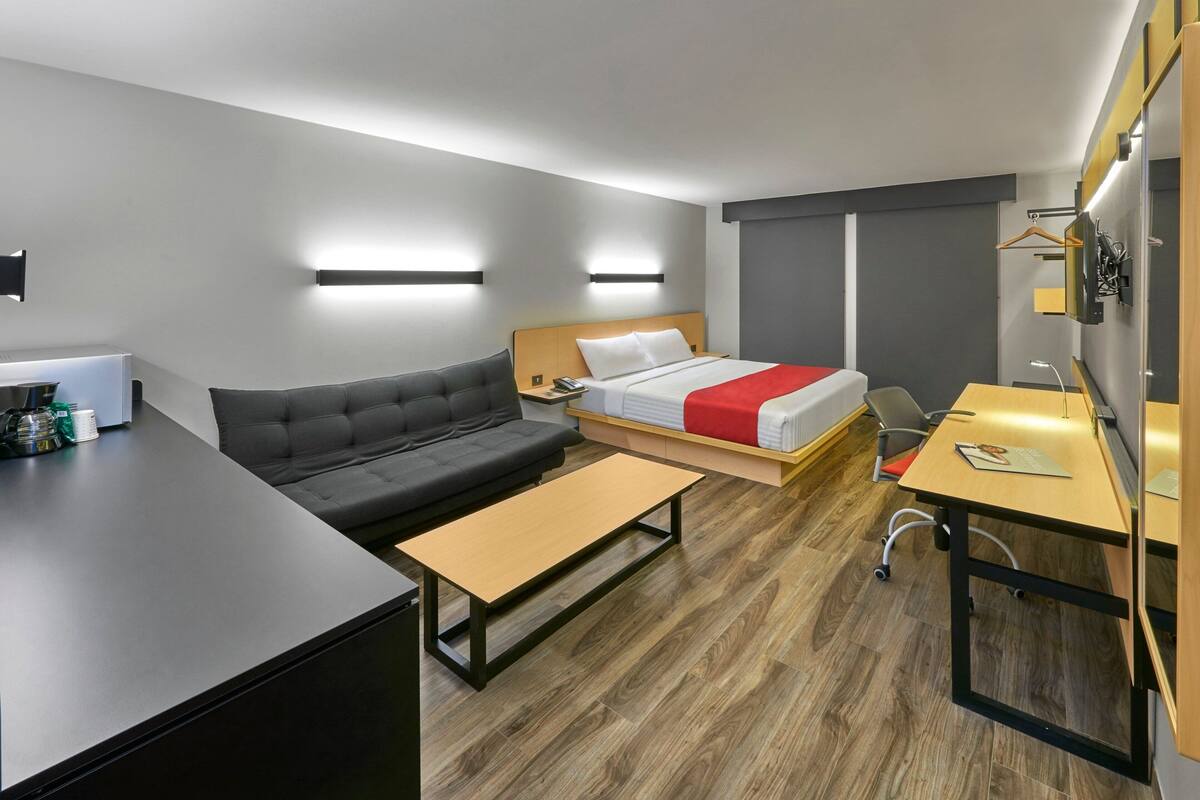 A modern hotel room with a bed, sofa, desk, and a small table.