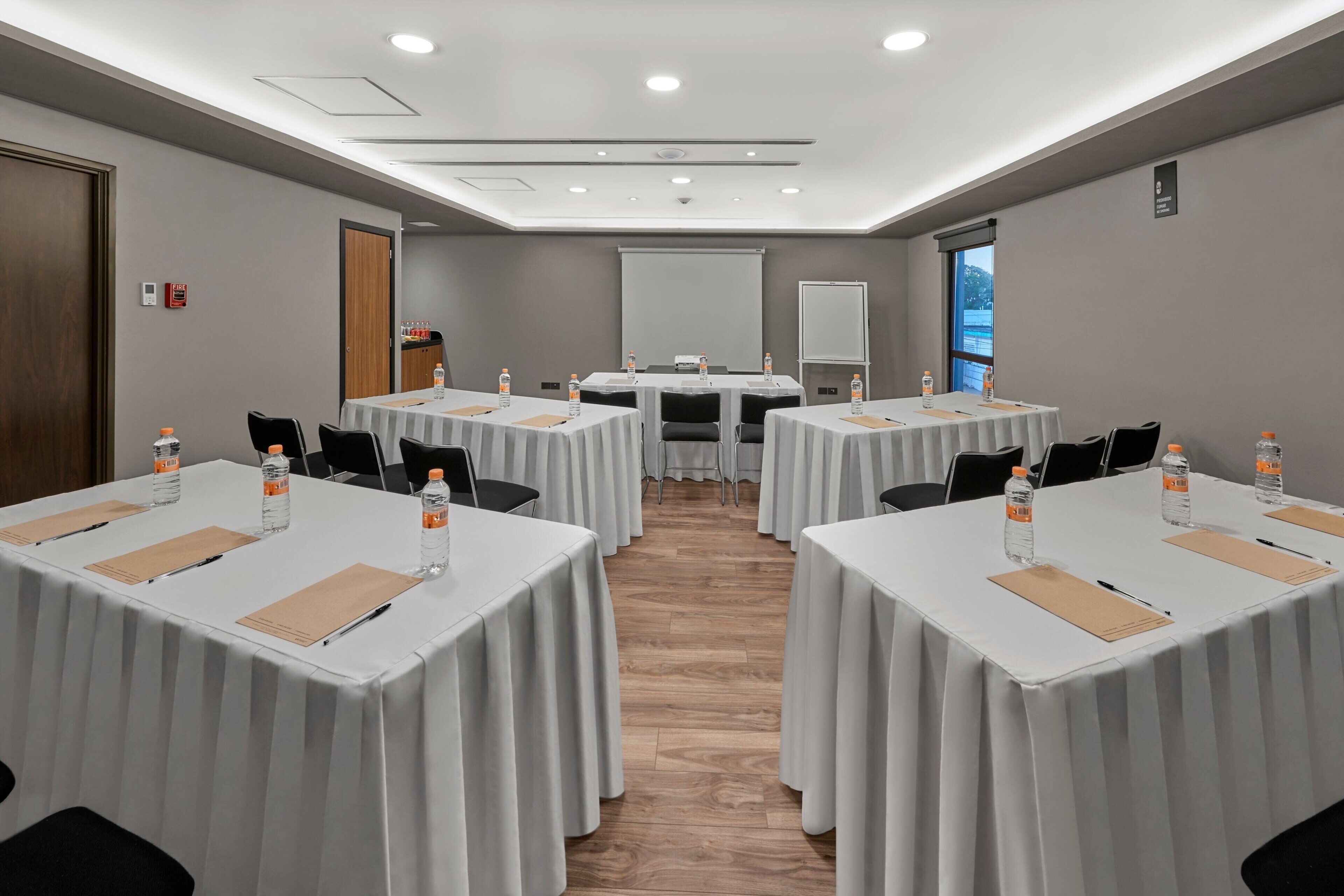 A conference room with multiple tables, chairs, and a projector screen.