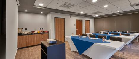 Un salón de conferencias con mesas largas, una kitchenette y un mostrador de recepción.