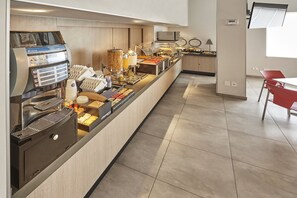 Un espace buffet avec une machine à café, divers aliments et une chaise rouge.