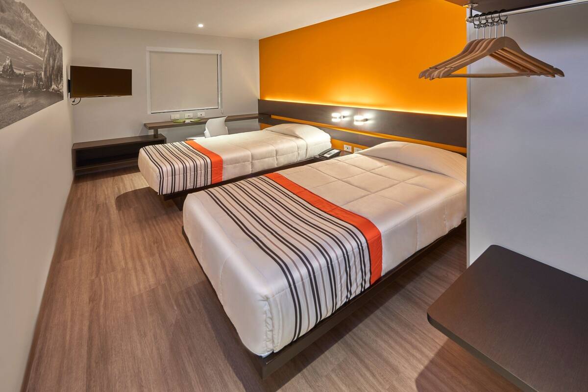 Een hotelkamer met twee bedden, een televisie, een bureau en een kapstok.