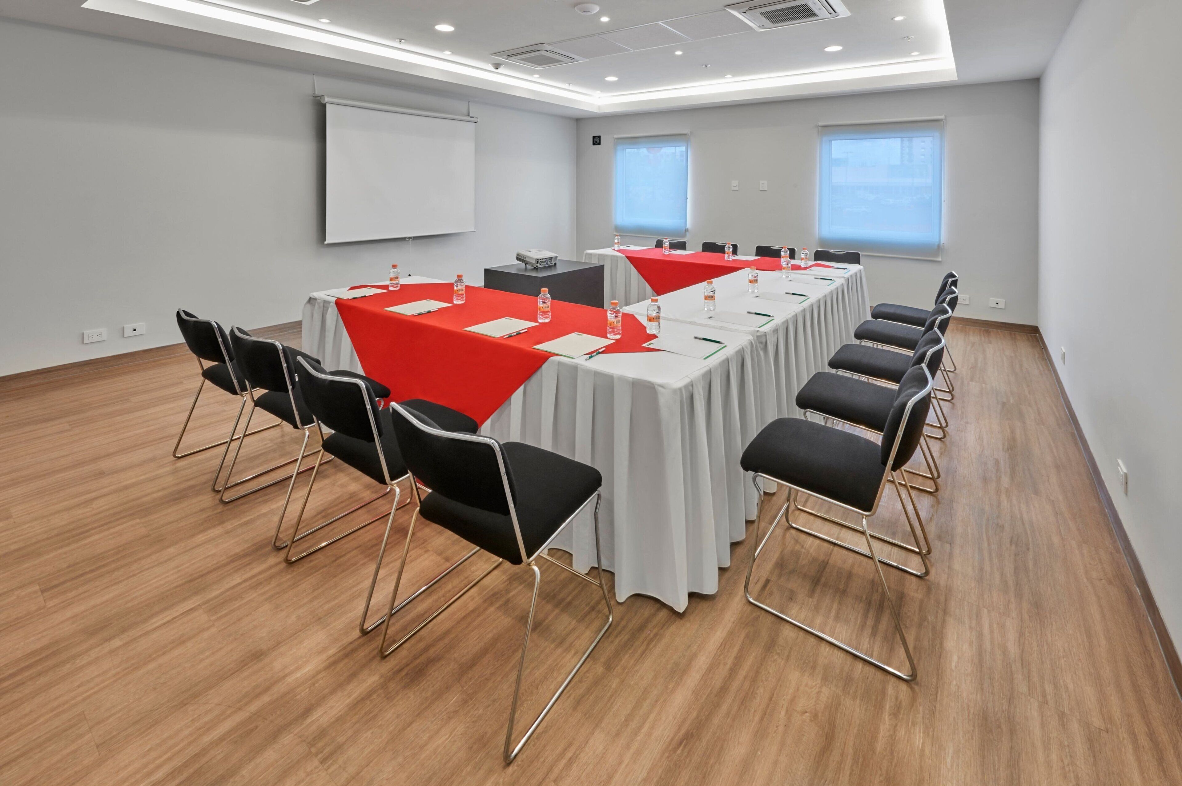 A conference room with a long table, black chairs, and a projector screen.