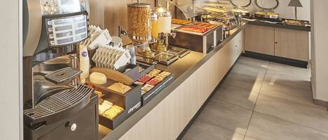 A buffet setup with a coffee machine, various food items, and a microwave.