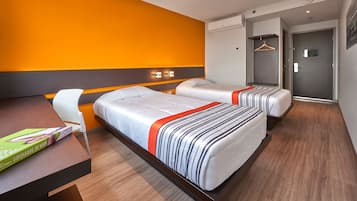 A hotel room with two beds, a desk, a chair, and an orange accent wall.