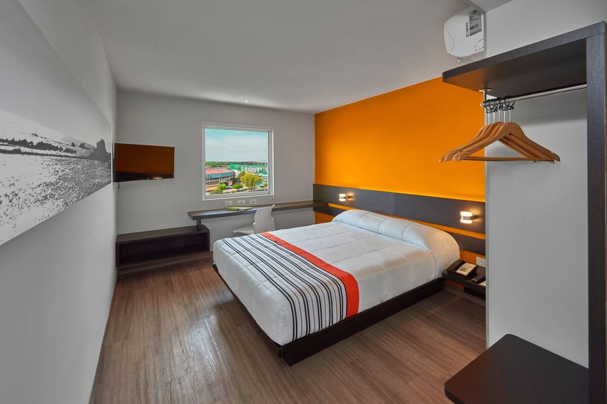 Een hotelkamer met een bed, een bureau, een stoel, een raam met uitzicht op de stad en een kapstok.