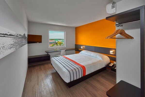 Una habitación de hotel con cama, escritorio, silla, ventana y vista a la ciudad, además de un perchero.
