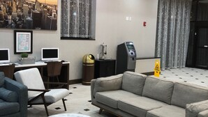 Eine Hotellobby mit einer Couch, Sesseln, einem Couchtisch, einer Karte, einem Stadtbildgemälde, einem Automaten und einem digitalen Kiosk.